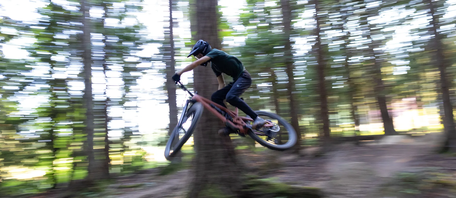 Mountain biker jumping on a trail through a pine forest, the background streaked with speed