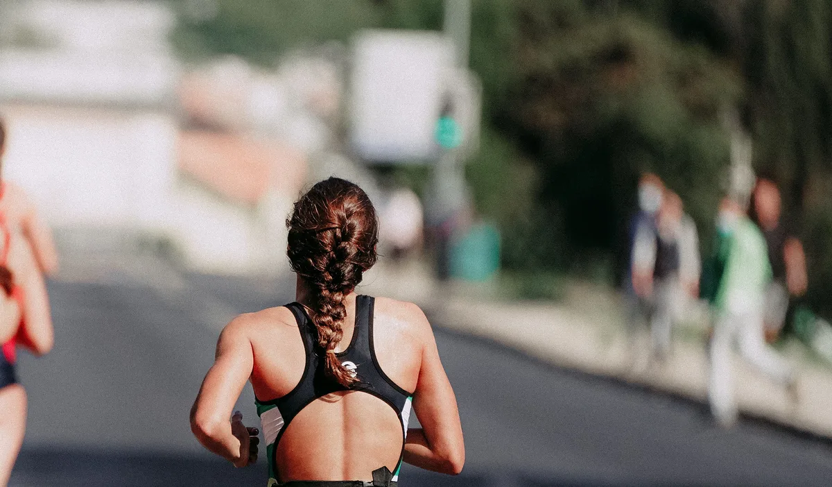 A runner from behind on an open road, the tarmac running away ahead of her