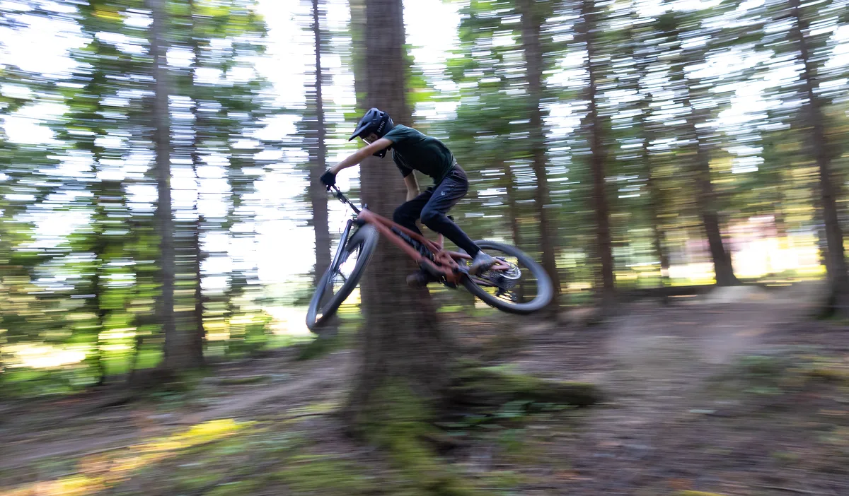 Mountain biker jumping on a trail through a pine forest, the background streaked with speed